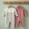Two striped baby onesies hanging on wooden hangers against a light green wall; white with navy stripes and pink with white stripes.