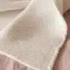 Cream-colored knitted blanket with a waffle-like texture draped over a pink wooden surface