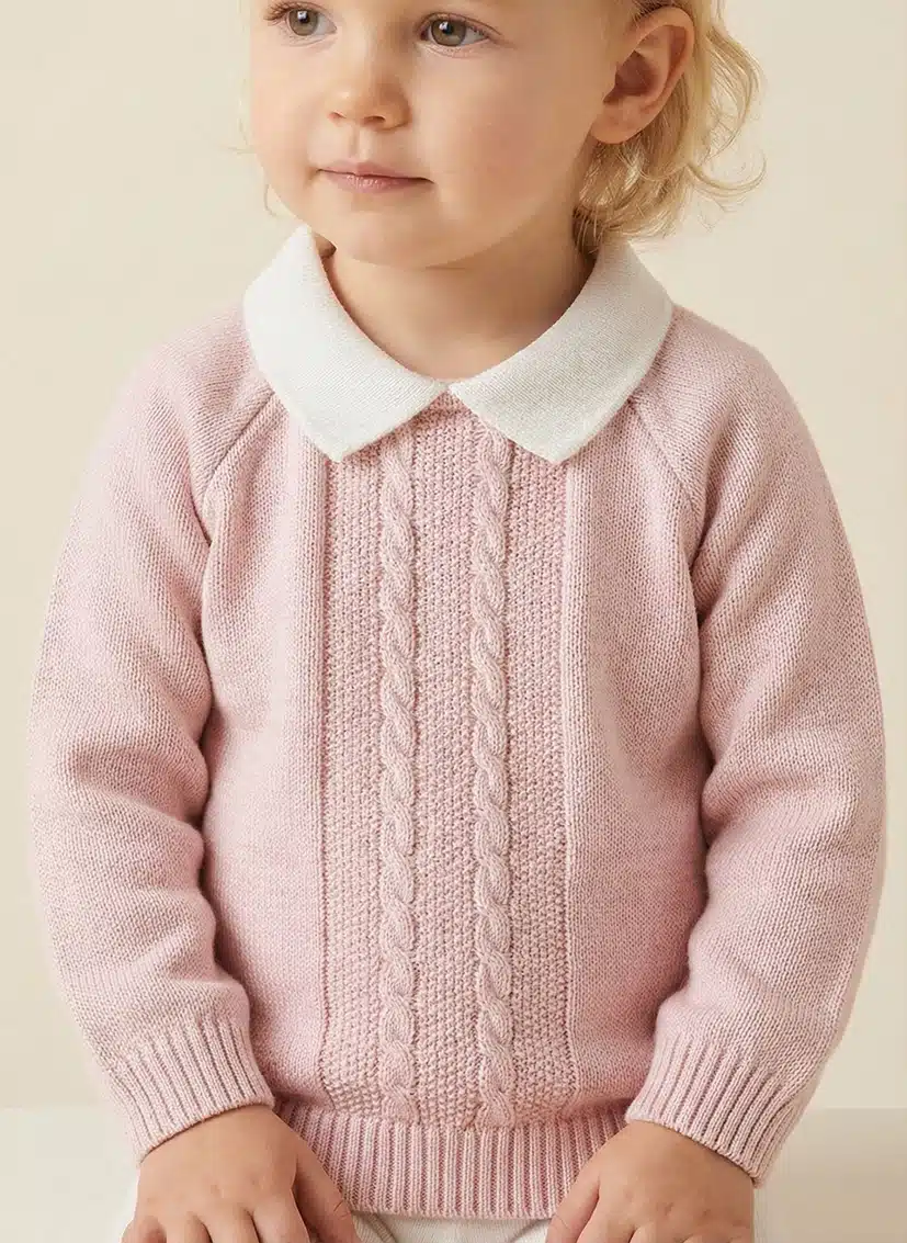 Young child wearing a soft pink knit sweater with a white Peter Pan collar, standing indoors.