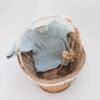 Blue knitted baby onesie folded in a wicker basket with a dried grass stem for a soft, cozy display.